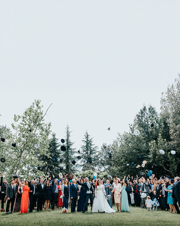 Sposi e invitati lanciano i cappelli in aria nel giardino del ristorante Le Case di Macerata durante un matrimonio all’aperto.